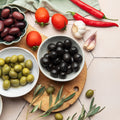 Assorted olives, tomatoes, and garlic on a wooden cutting board with a light background.