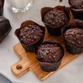 Chocolate muffins on a wooden board with scattered chocolate chips on a marble surface.