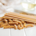 Dried pasta on a white wooden surface with a glass of white wine in the background.