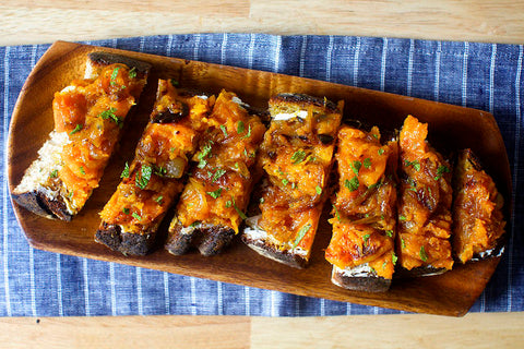 Roasted butternut squash on toast. Plated on a wooden board on a table.
